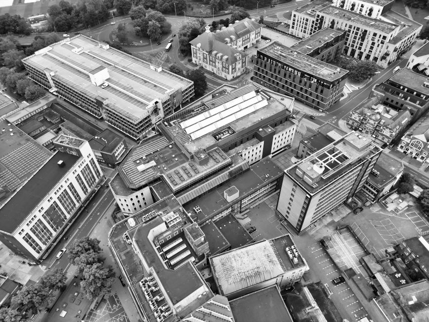 An aerial black-and-white photograph of a dense urban area in Chelmsford, featuring modern office buildings, commercial structures, and parking lots. The buildings vary in height and architectural sty
